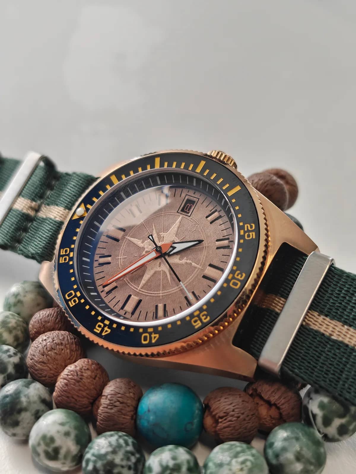 El reloj apoyado sobre las pulseras de cuentas de madera y turquesa, con la correa NATO verde y caqui