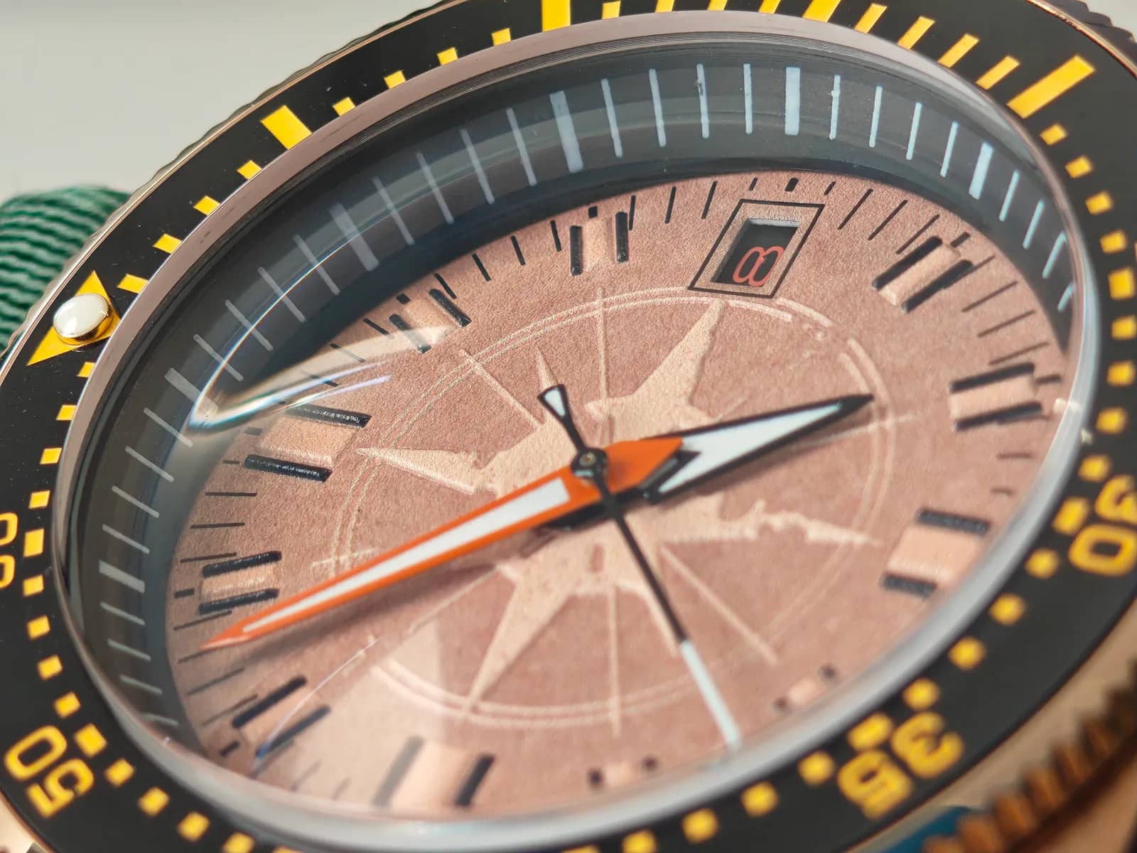 Macro de la carátula: la rosa de los vientos en relieve, la manecilla de minutos naranja y el disco de fecha negro con números naranja