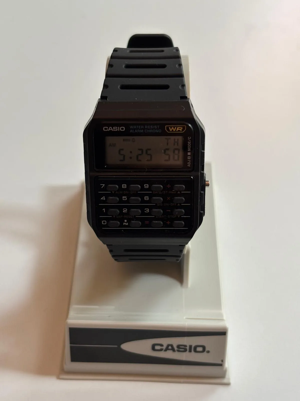 El Casio CA-53W-1ER de frente: pantalla LCD con la hora y el día, insignia WR dorada y el teclado completo de la calculadora