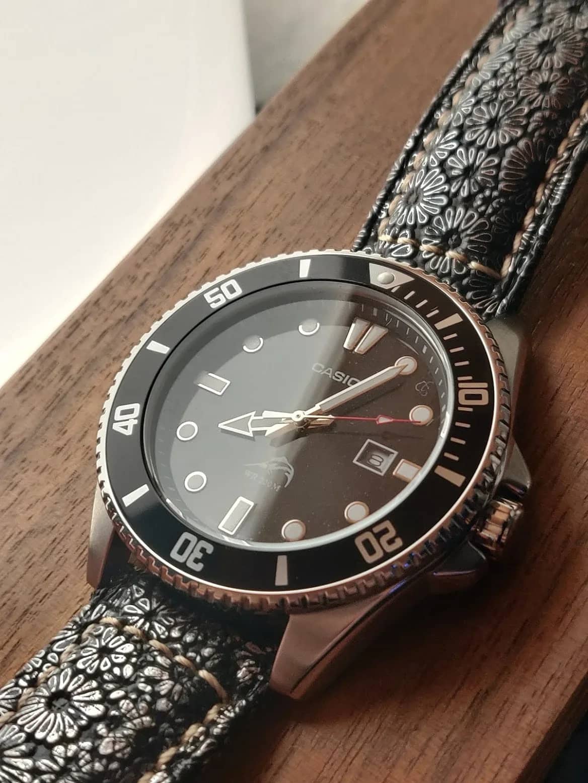 El Casio Duro sobre madera con una correa de cuero negro repujado de flores y costura beige