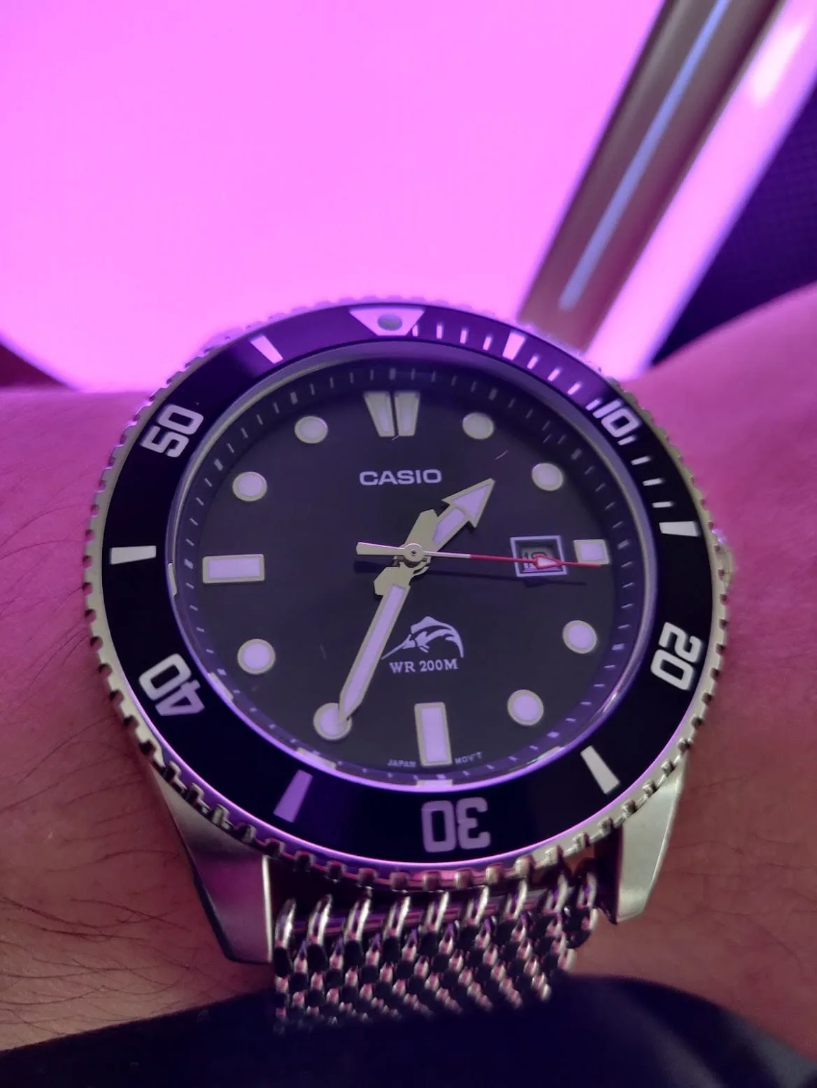El MDV106 con brazalete de malla bajo luz magenta: el bisel y los índices teñidos de rosa