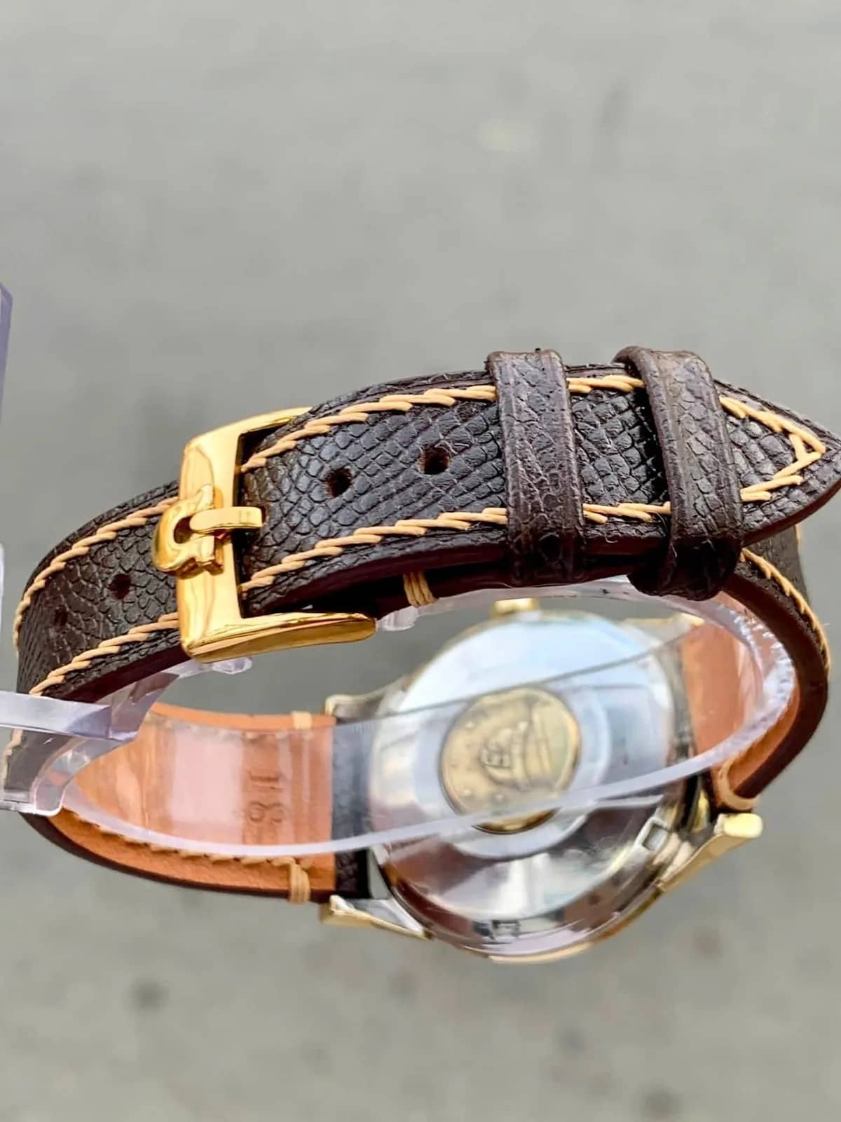 La hebilla dorada firmada Omega sobre la correa de piel marrón con costura beige