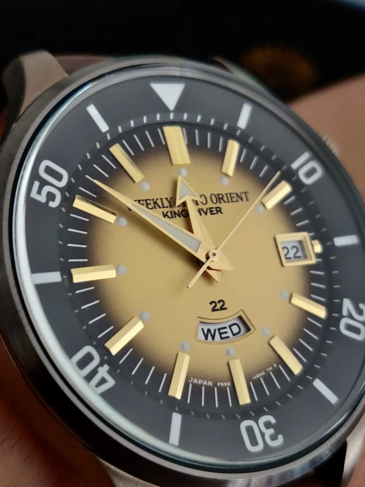 Macro de la esfera dorada en degradado: la firma «Weekly Auto Orient King Diver», la fecha a las 3 y el día a las 6