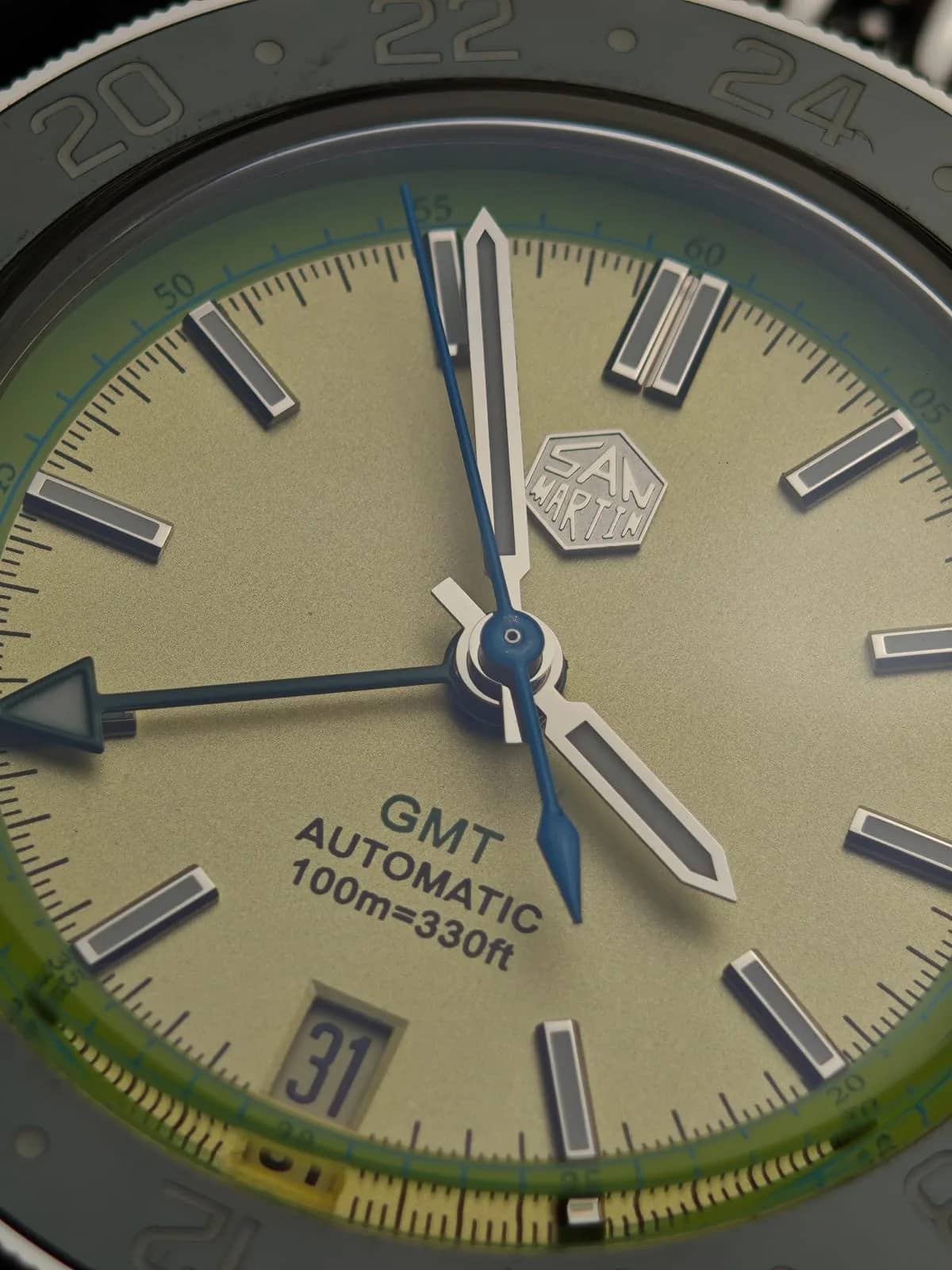 Macro del dial: logotipo hexagonal de San Martin aplicado, agujas con lumen y segundero azul
