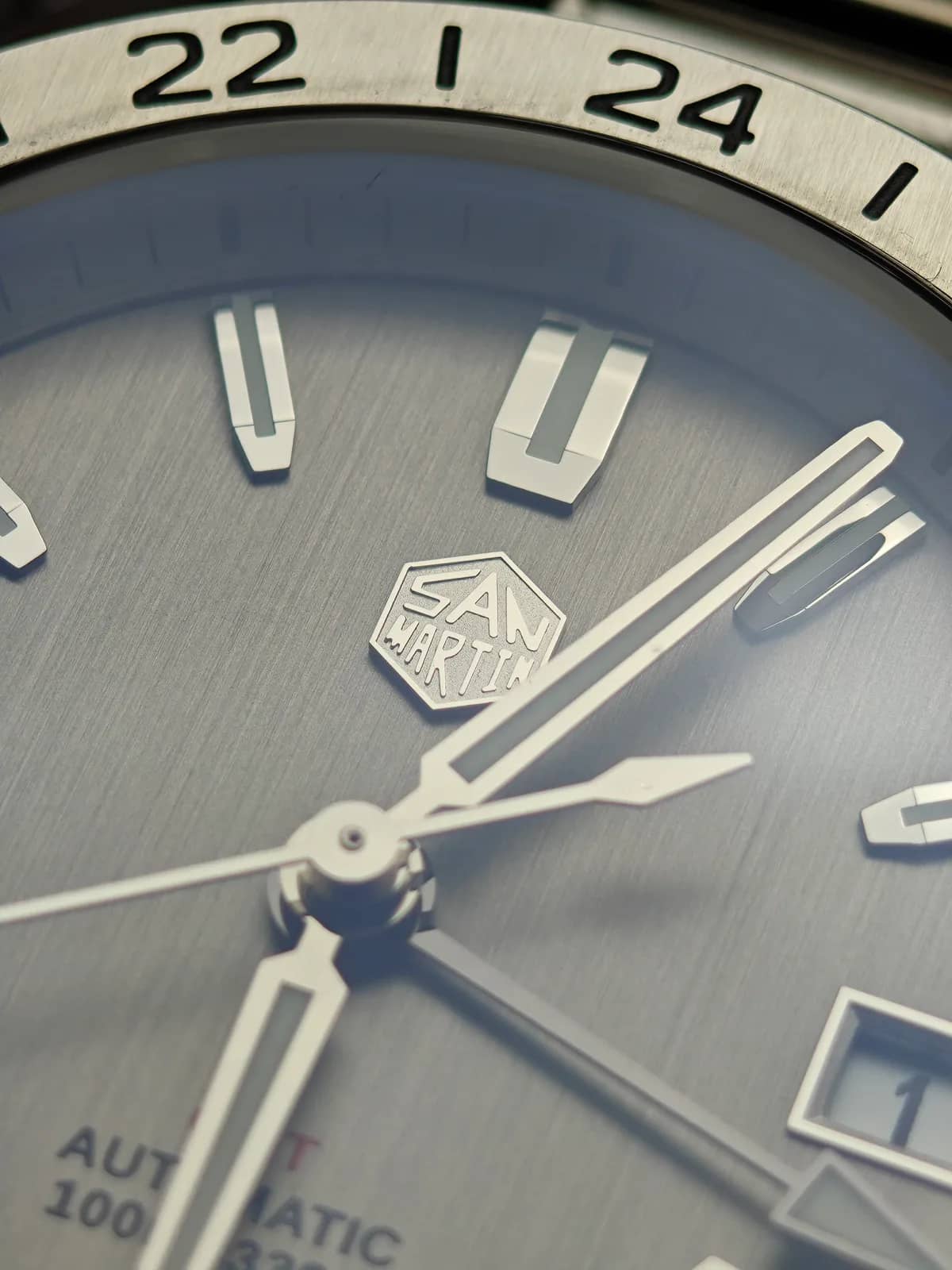 Detalle de los índices dobles a las 12 y el logo hexagonal, con el bisel de 24 horas desenfocado