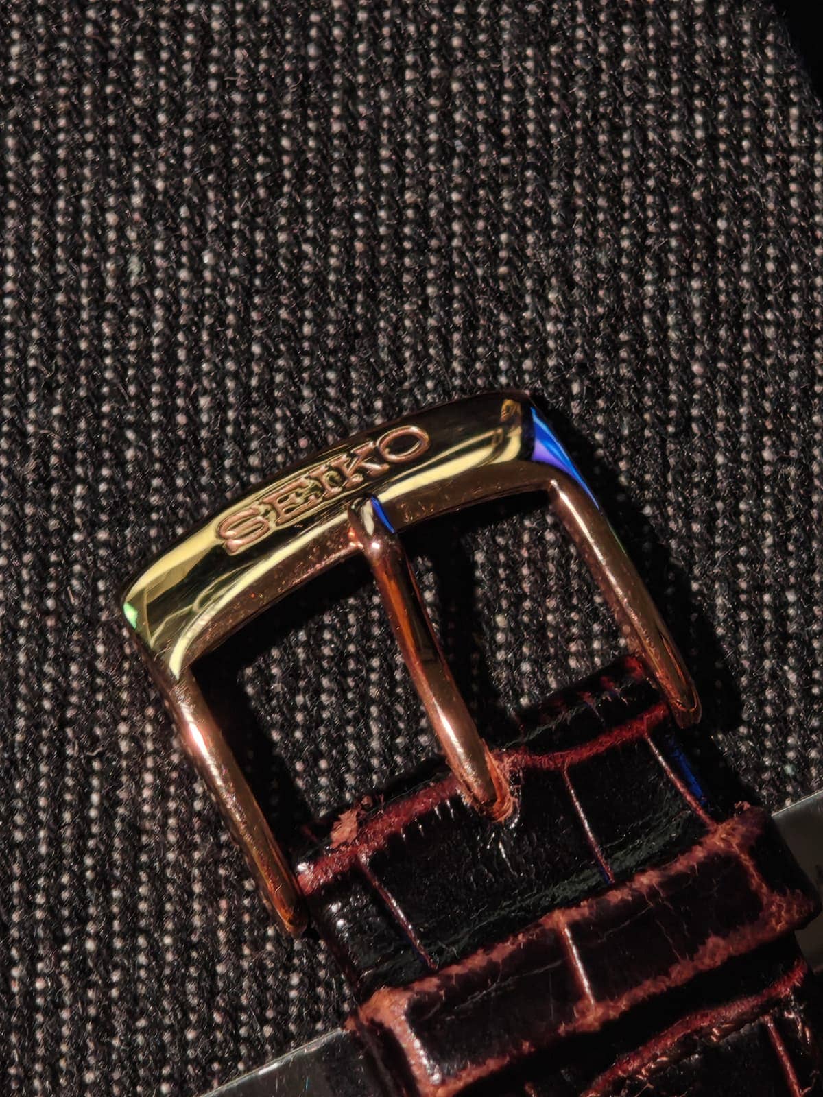 La hebilla en tono oro rosa con el grabado SEIKO, sobre la correa marrón con textura de cocodrilo
