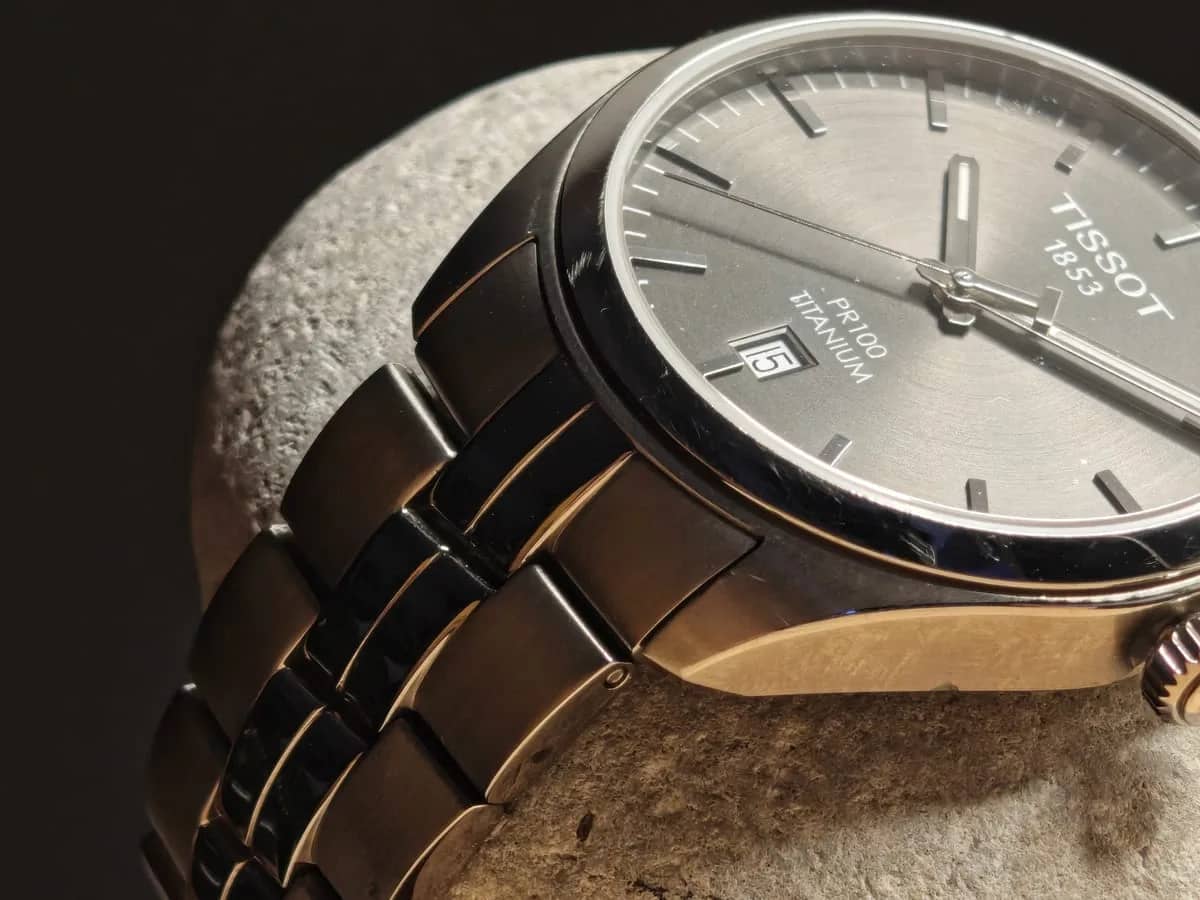 El brazalete de titanio de eslabones alternos conduce la mirada hasta la esfera antracita del PR 100, con el logotipo Tissot 1853