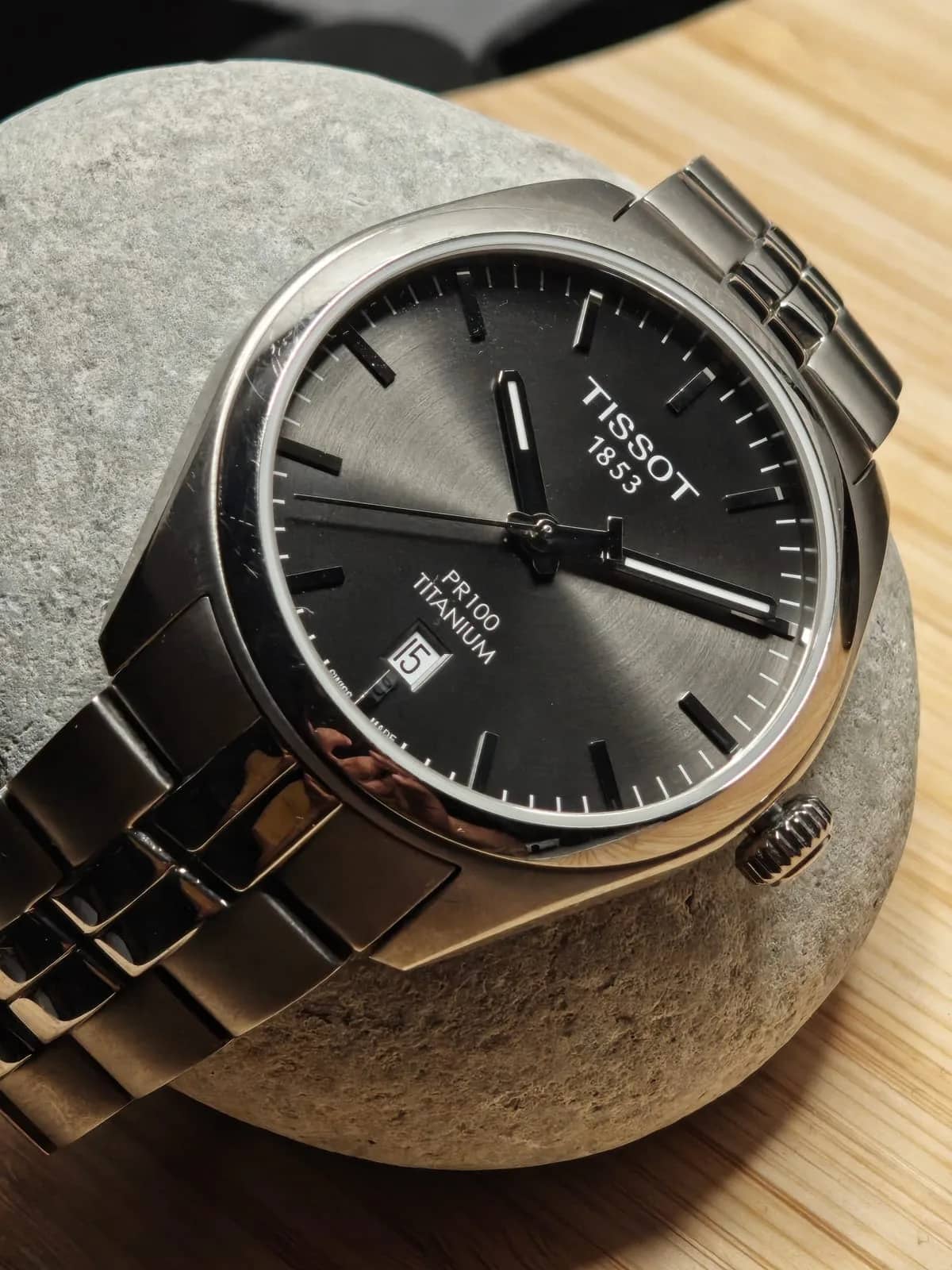 Primer plano del dial antracita: agujas bastón con franjas luminiscentes, minutero ferroviario y firma PR100 Titanium