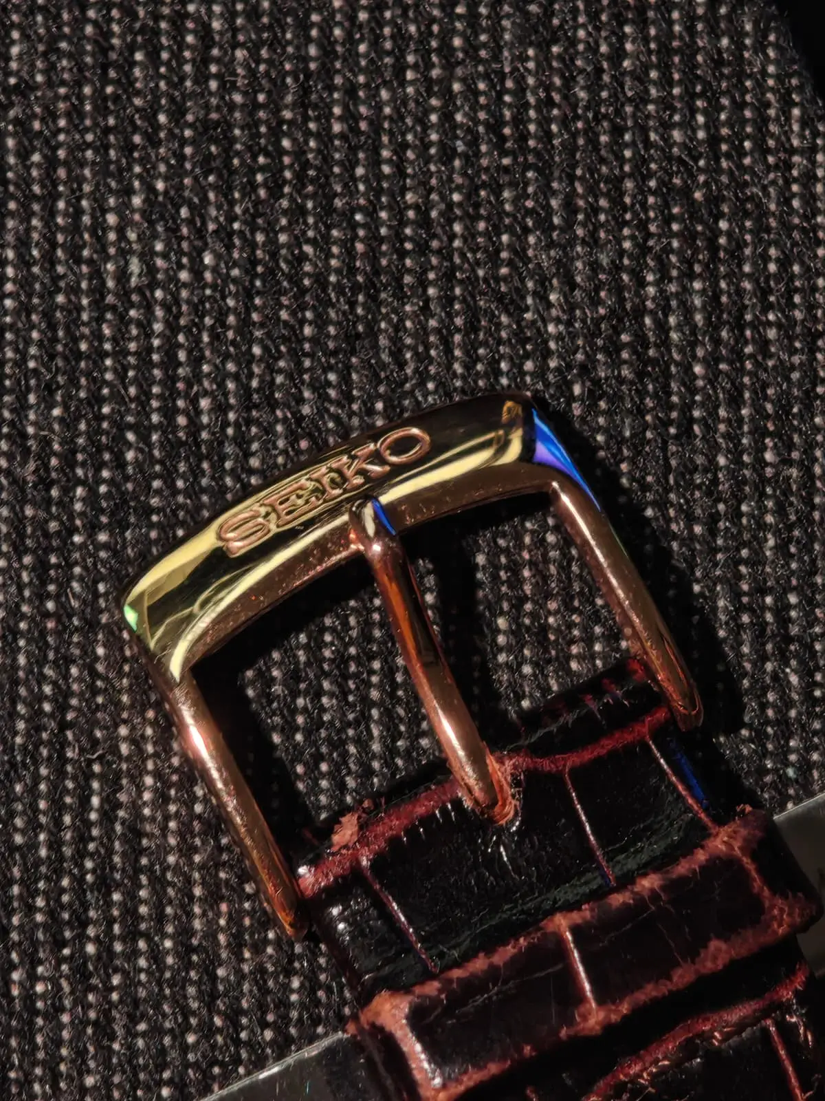 La hebilla en tono oro rosa con el grabado SEIKO, sobre la correa marrón con textura de cocodrilo